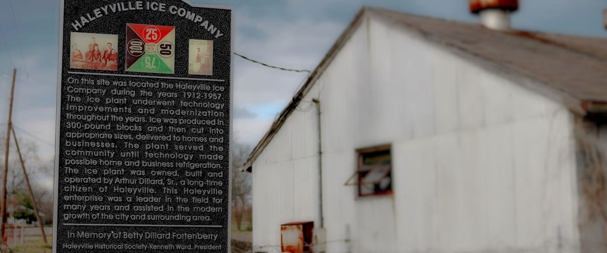 A historical signboard with information about the Haileyville Ice Company, located in front of an old, weathered building.
