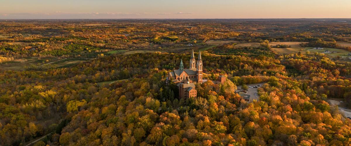 An aerial view of a church surrounded by autumn-colored trees.