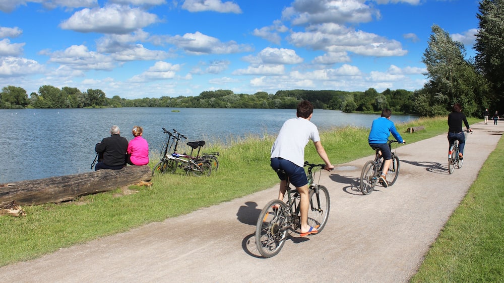 A lakeside path with cyclists and a couple sitting on a log.