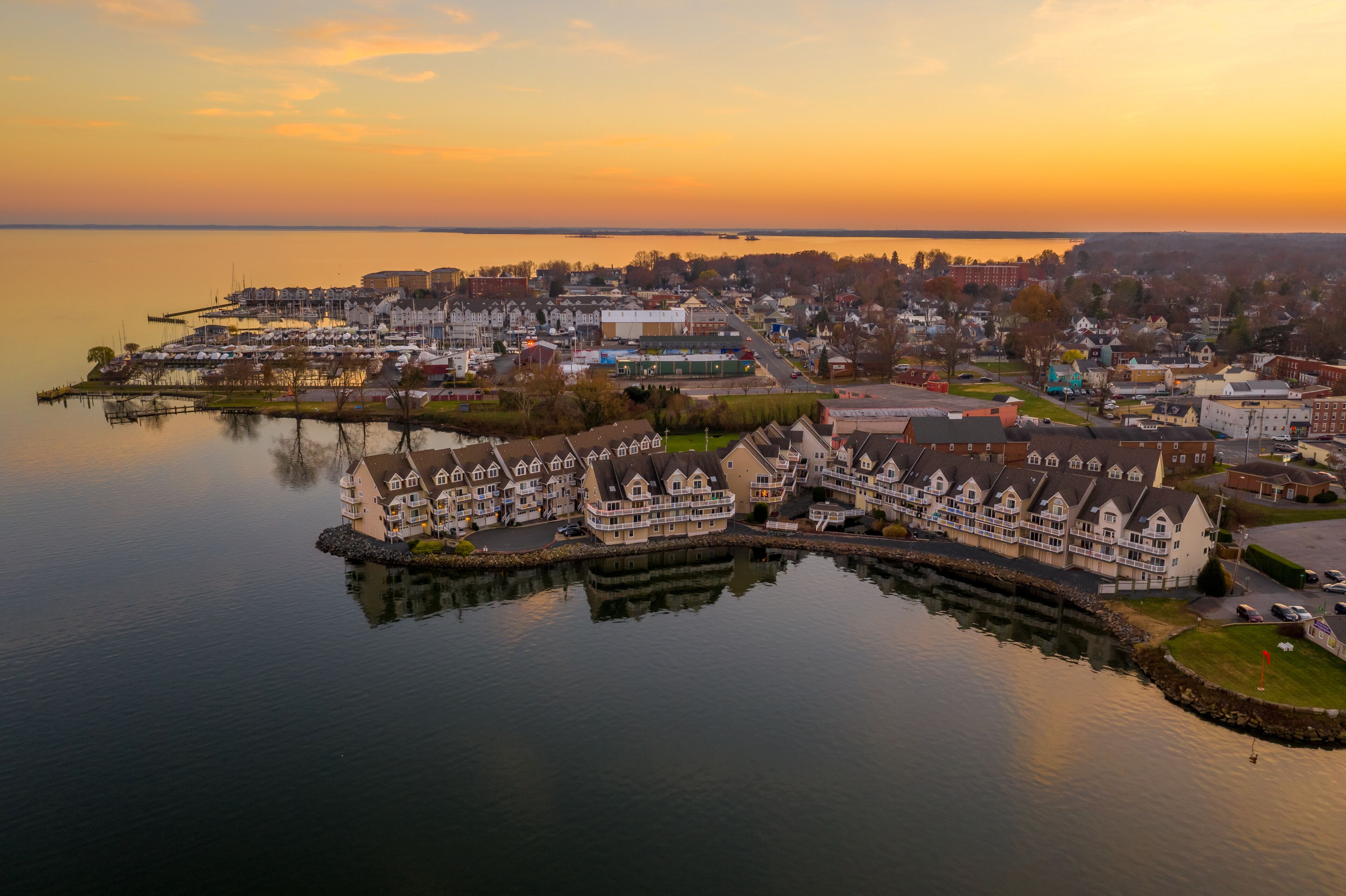 Aerial view of downtown Havre de Grace in Maryland with luxury waterfront apartment complex reflecting in the water as the sun paints the sky orange