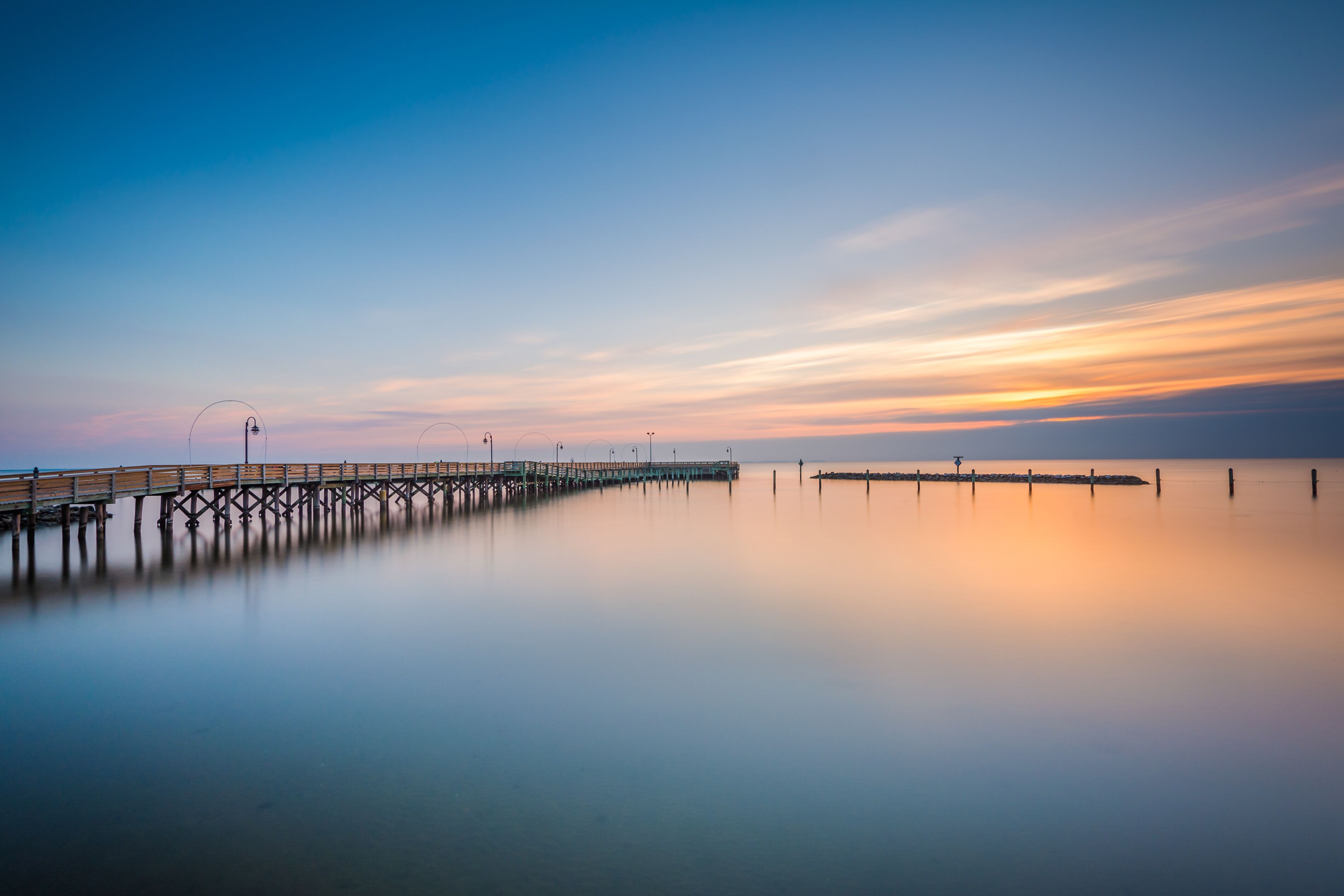 A long pier extending into calm waters with a clear sky above.