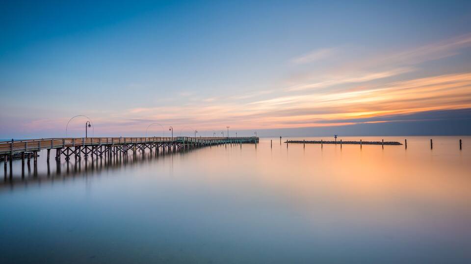 A long pier extending into calm waters with a clear sky above.