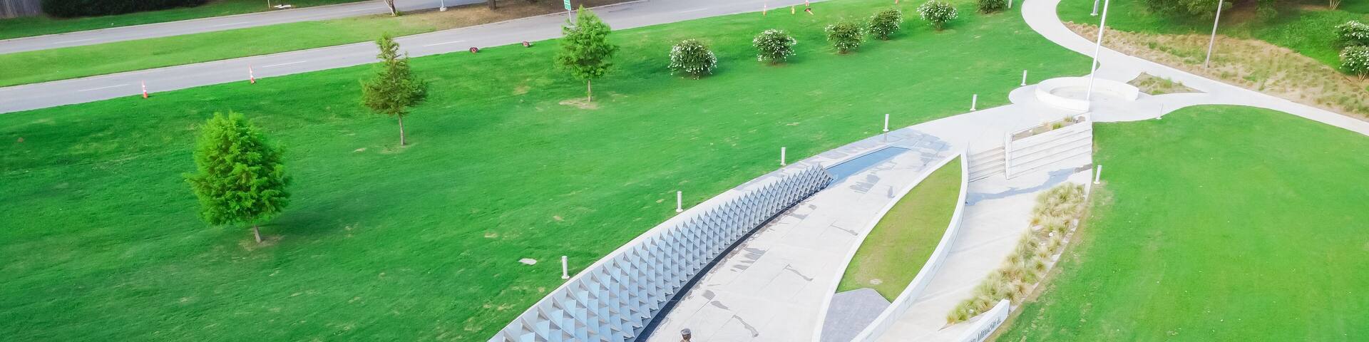 Aerial view kids playing in water fountain, reflecting pool at Doris Miller Memorial in Waco, Texas, metal panel installation representing of USS West Virginia in WWII, sculpture
