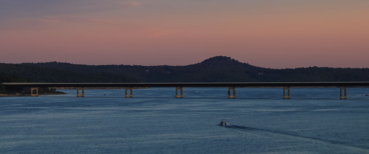 A bridge over a body of water with a hilly landscape in the background.