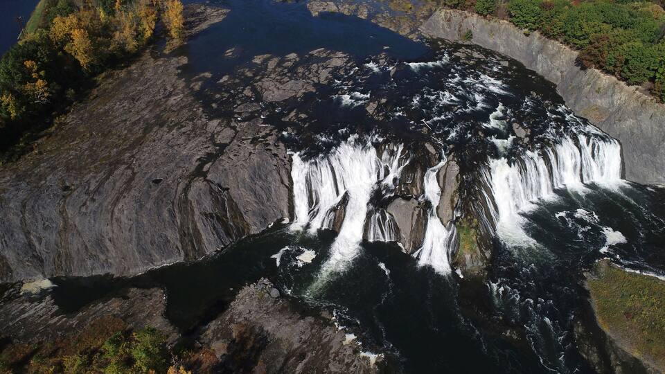 A waterfall cascading over a rocky cliff into a river.