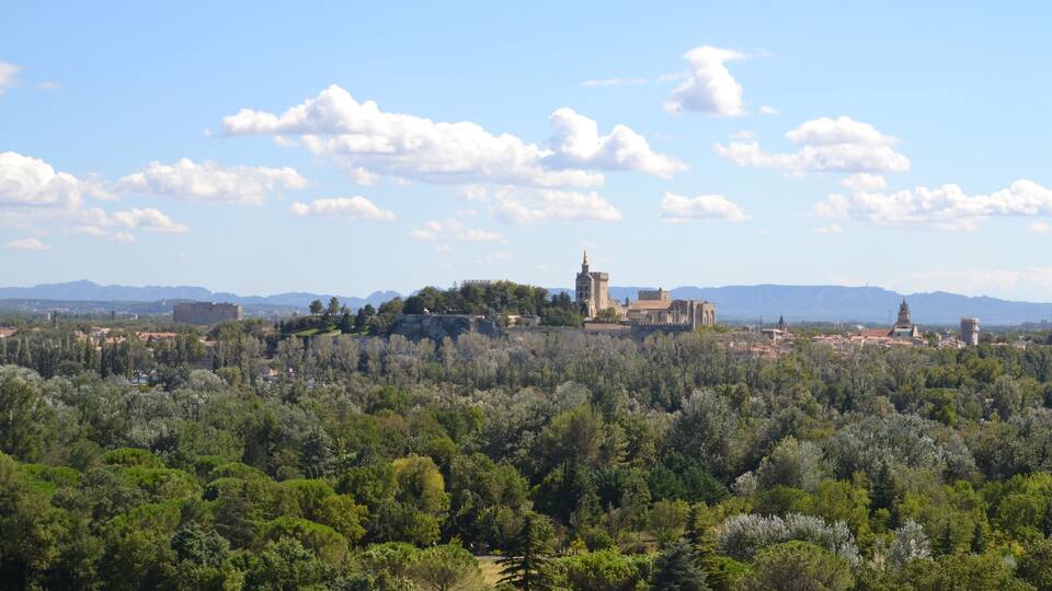 A historic town with a prominent church on a hill, surrounded by dense green forests and distant mountains.