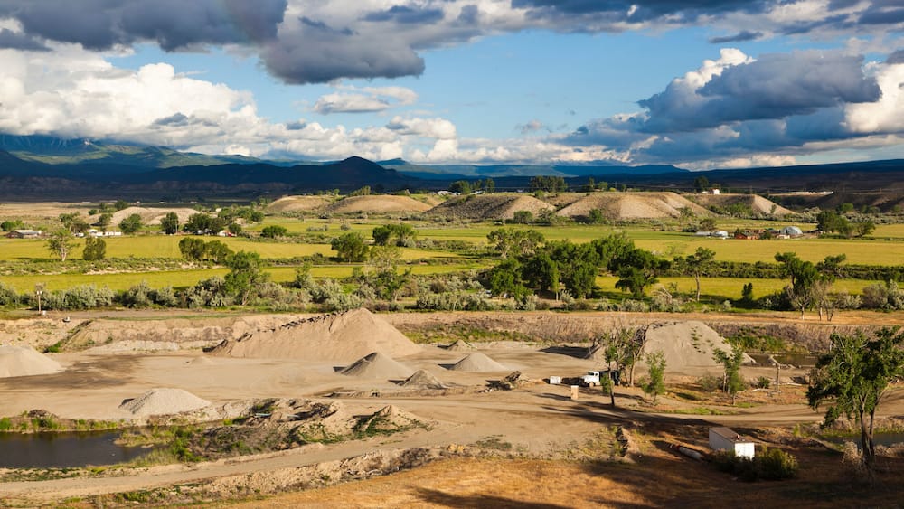 A rural landscape with rolling hills, a dirt road, and scattered buildings.