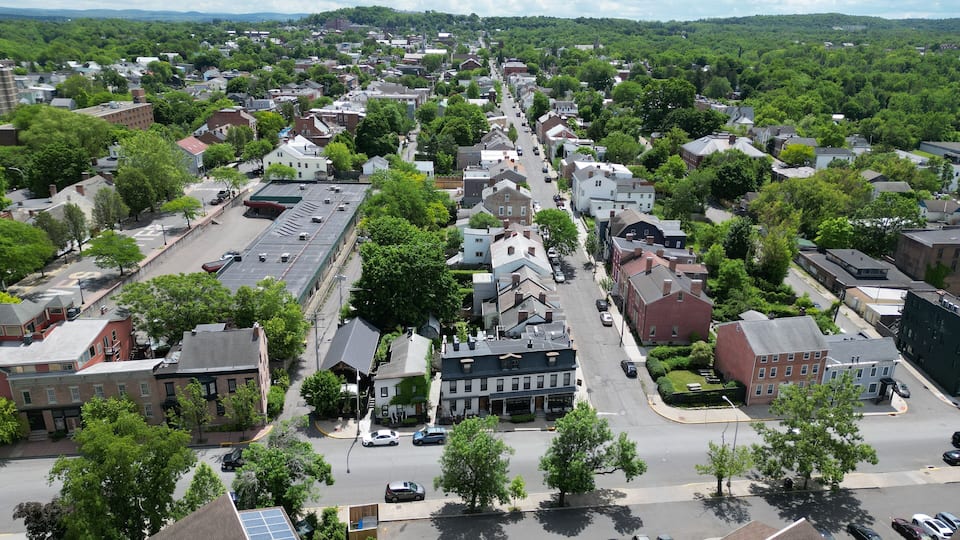 aerial view of hudson, new york (small hudson valley town city downtown historic district) mountains catskills ny travel destination main street with hills clouds cars tree matter