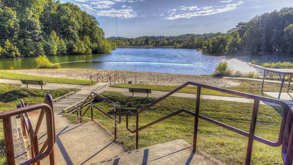 A lakeside park with a concrete staircase, metal railings, and picnic tables.
