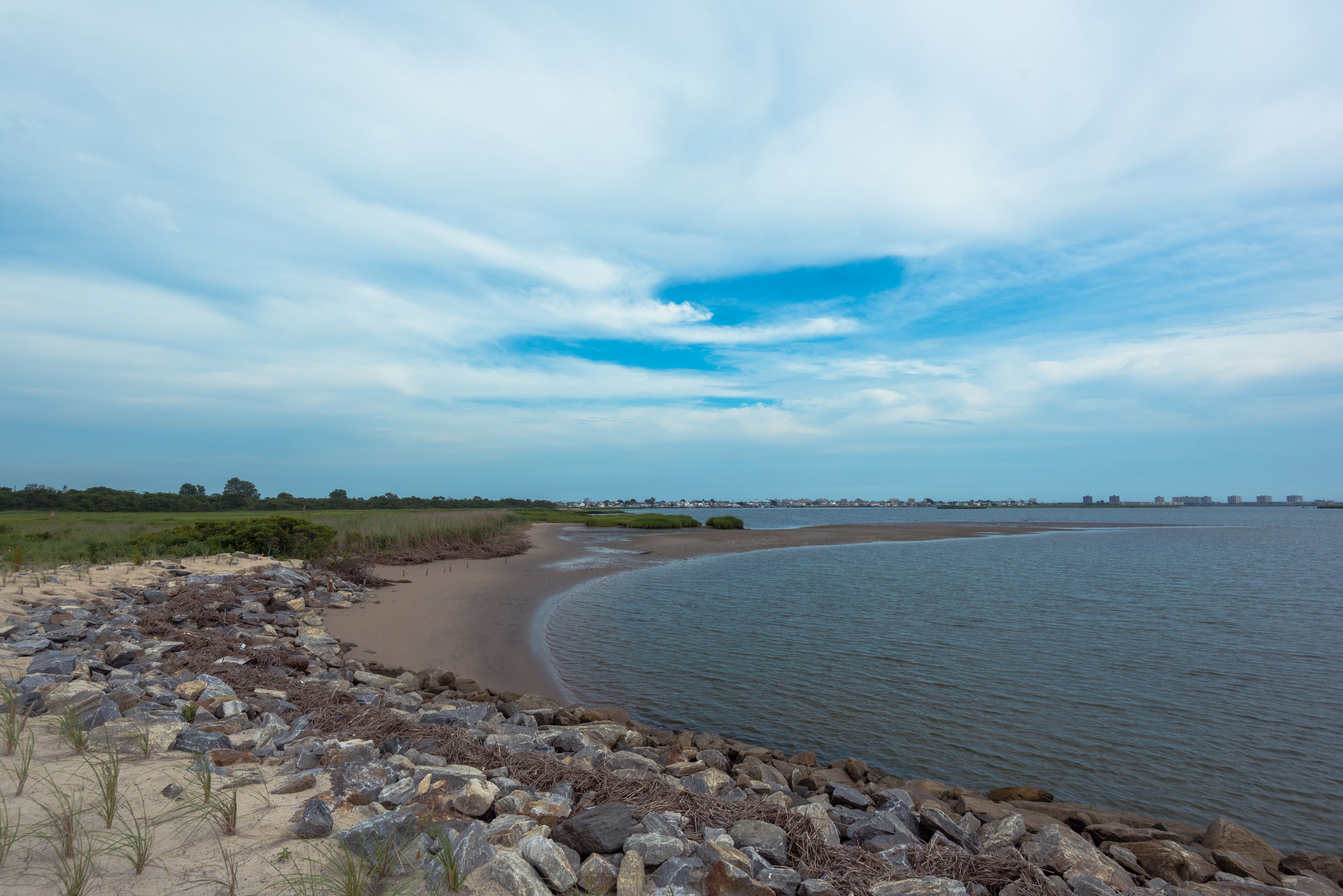 A coastal landscape with a sandy beach, rocky shoreline, and a calm body of water.