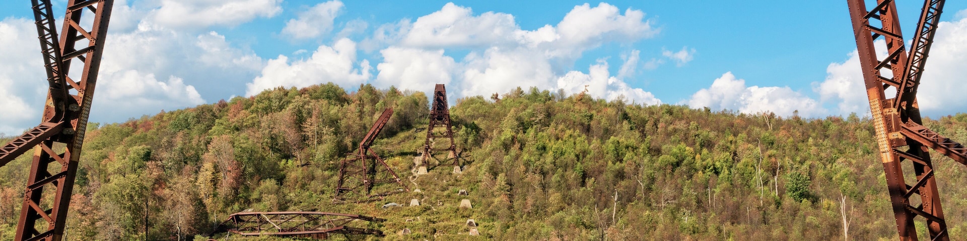 Una estructura de puente metálico oxidada, con una colina boscosa al fondo.