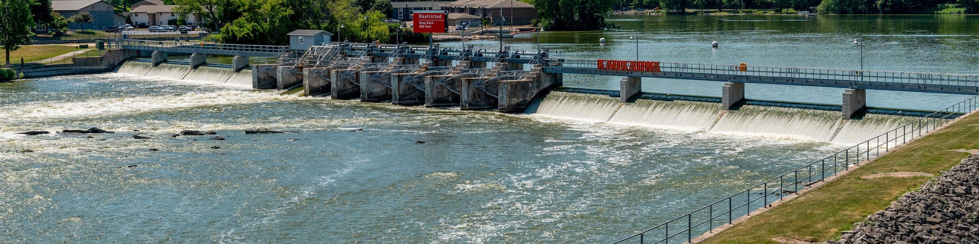 A dam with water flowing over it, a bridge, and a river with surrounding greenery.