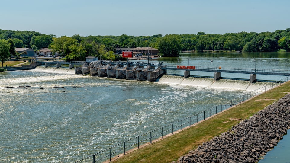A dam with water flowing over it, a bridge, and a river with surrounding greenery.