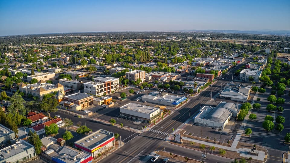 An aerial view of a city with a mix of commercial and residential buildings, wide streets, and green spaces.