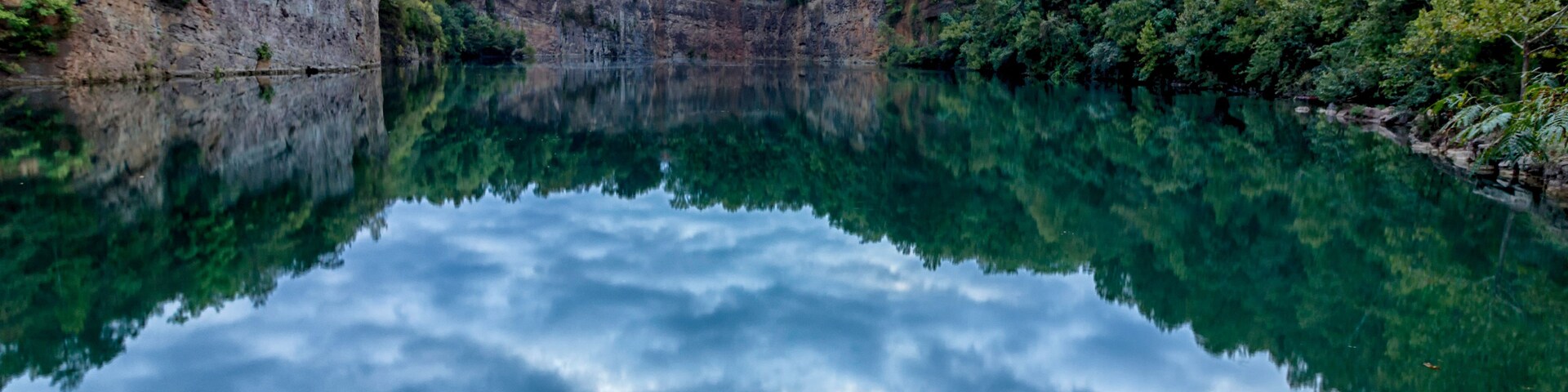 A calm lake reflecting the surrounding cliffs and dense forest.