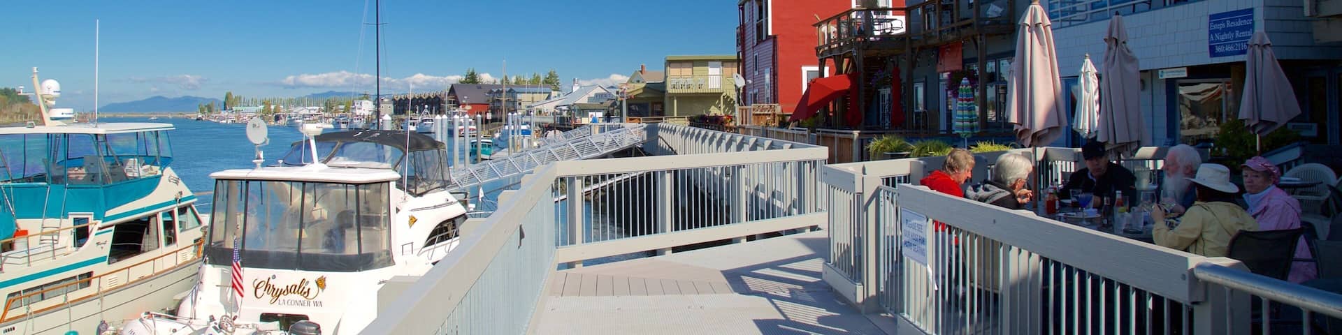A marina with boats docked, a pedestrian bridge, and buildings with outdoor seating.