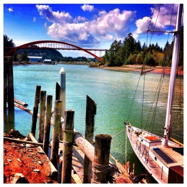 A river with a wooden dock and a red bridge in the background.