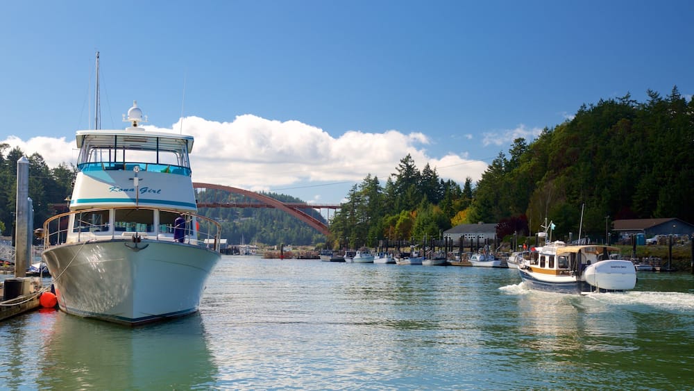 A boat named 'Kona Girl' docked at a marina with a forested hillside in the background and a bridge in the distance.