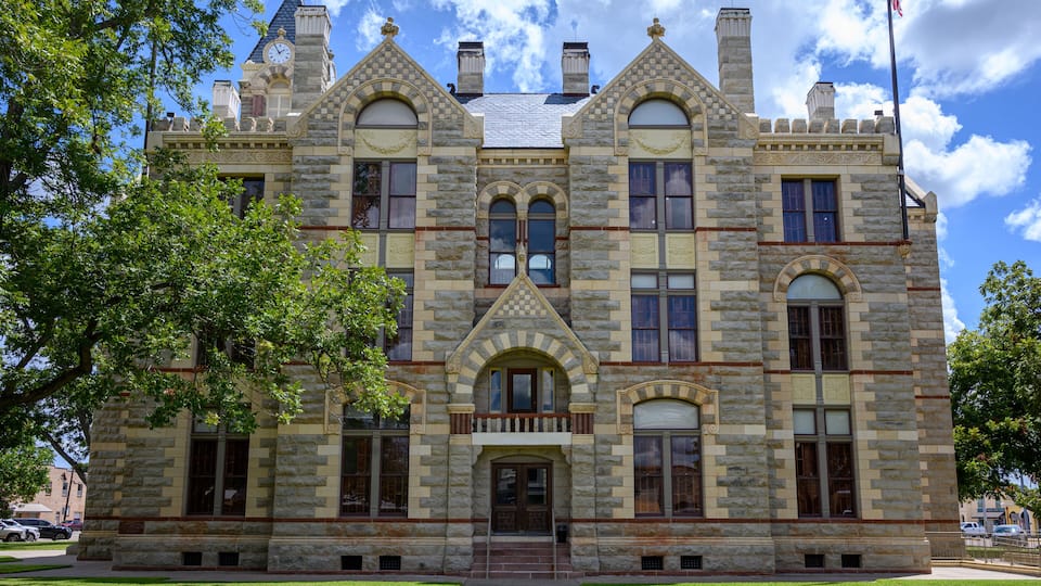A large stone building with a clock tower, arched windows, and a flagpole.