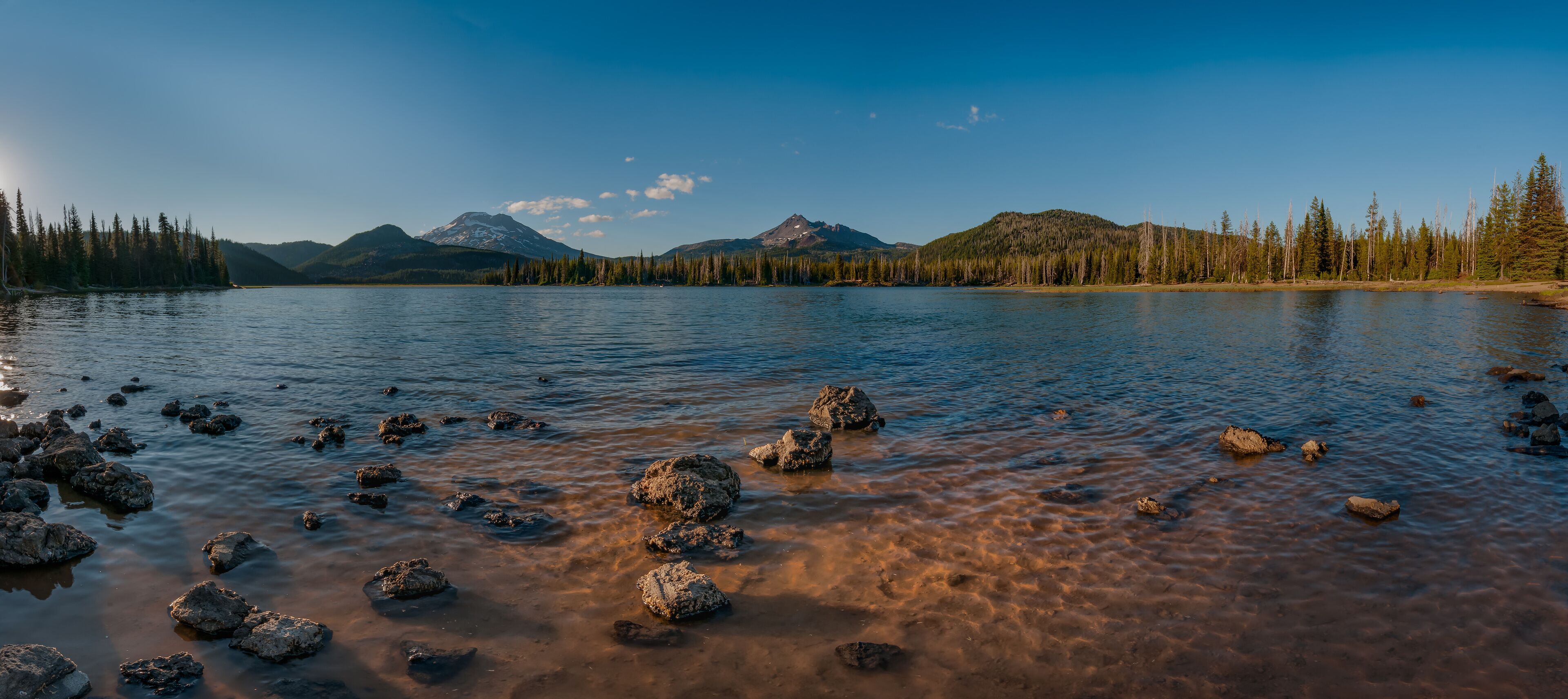 Rocky lakeshore with mountain peaks and blue sky in distance