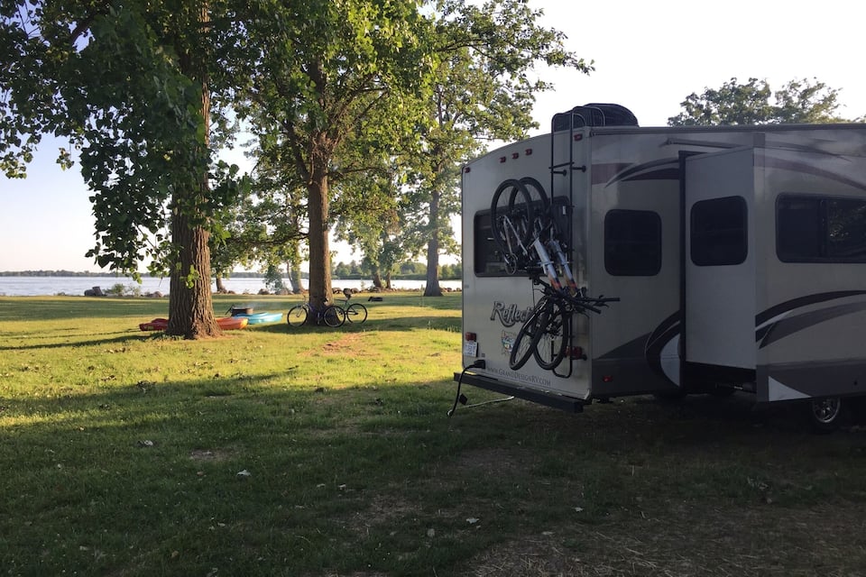A recreational vehicle parked in a grassy area with trees and a lake in the background.