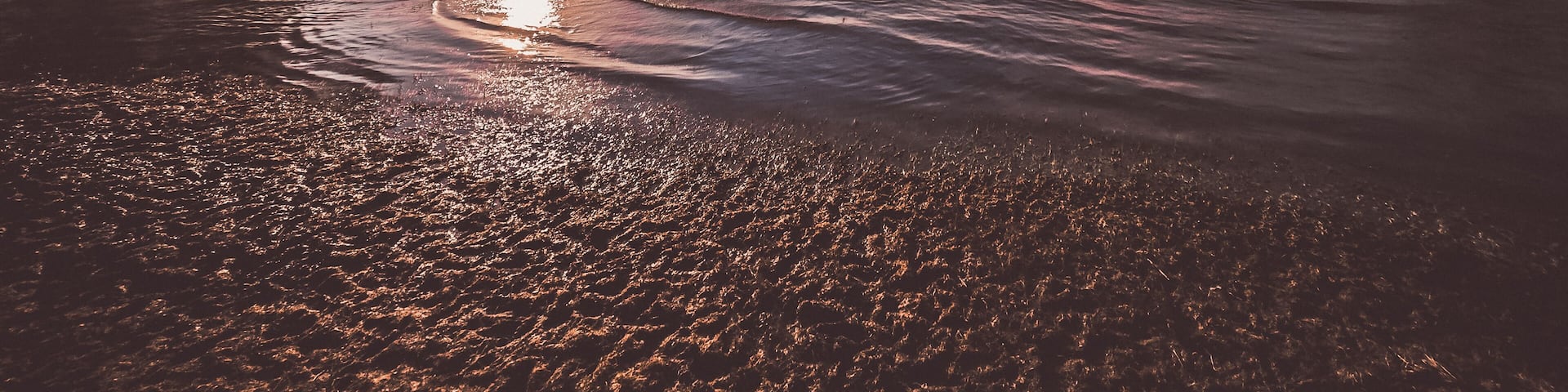 Sunshine over a calm lake with reflecting water and a vast sky. The sandy beach in the foreground invites relaxation.