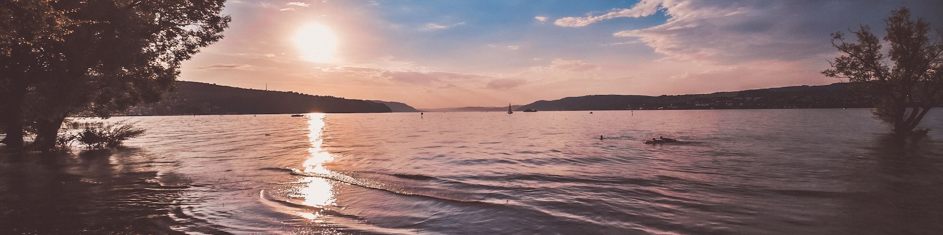 Sunshine over a calm lake with reflecting water and a vast sky. The sandy beach in the foreground invites relaxation.