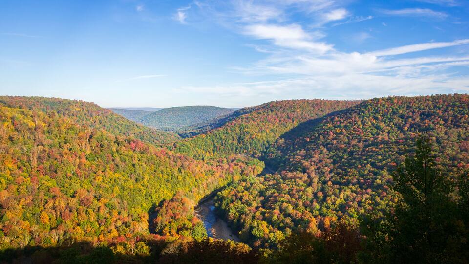 A valley with a river, surrounded by hills covered in autumn foliage.