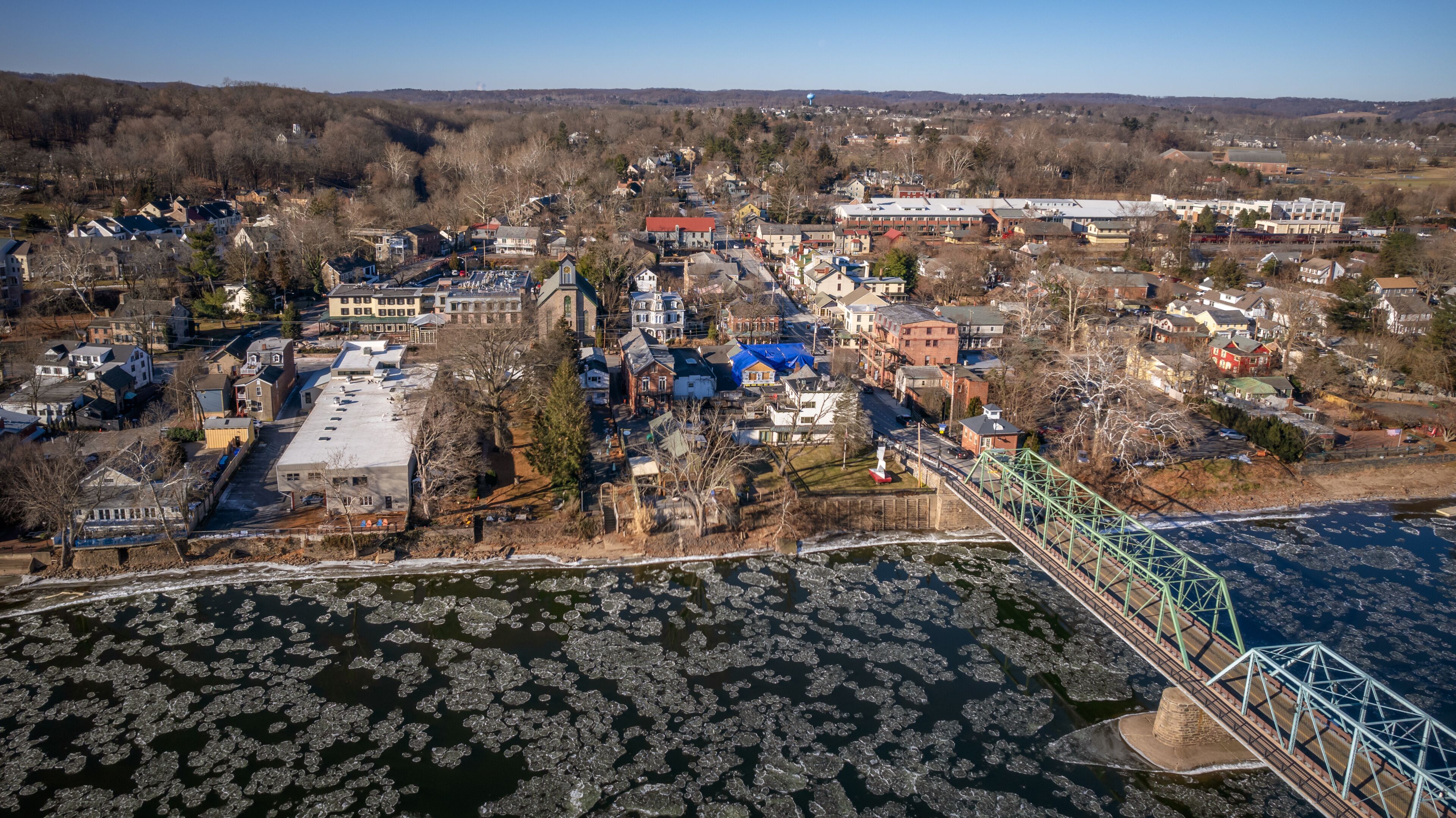 An aerial view of a town with a river, ice floes, and a bridge.