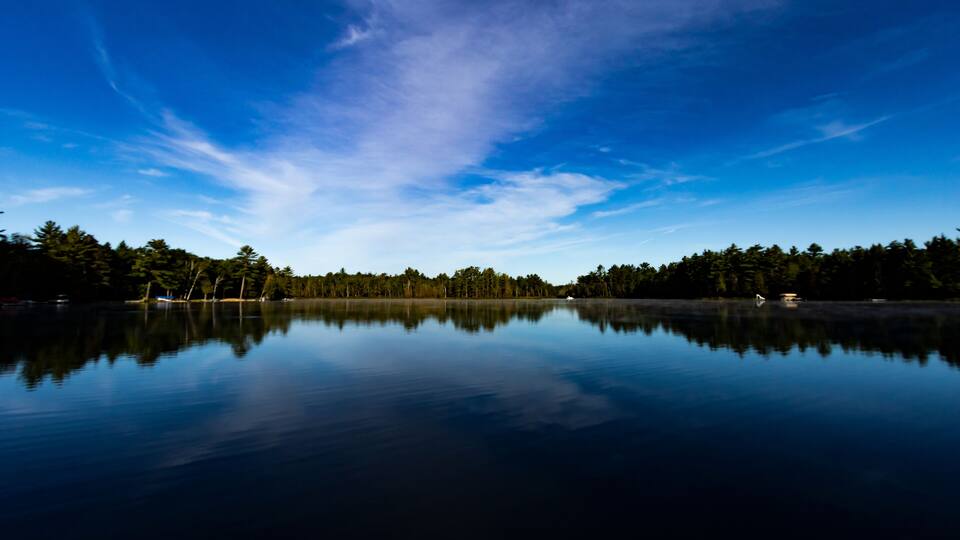 A calm lake with a clear reflection of the sky and trees.