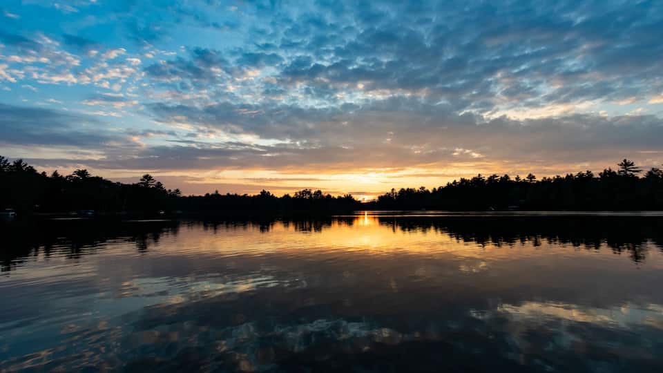 A sunset over a calm lake with a forested shoreline.