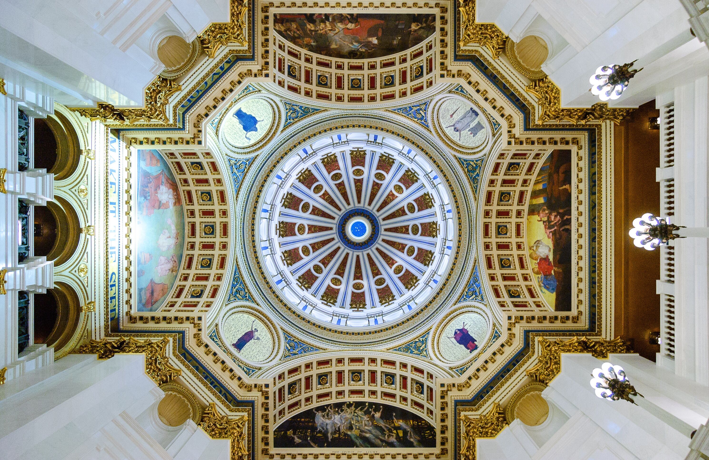 Un techo suntuoso y ricamente decorado, con un diseño circular central, rodeado de detalles intrincados en dorado y frescos.
