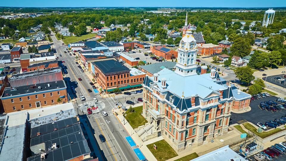 An aerial view of a town with a prominent clock tower, a large water tower, and a mix of historic and modern buildings.