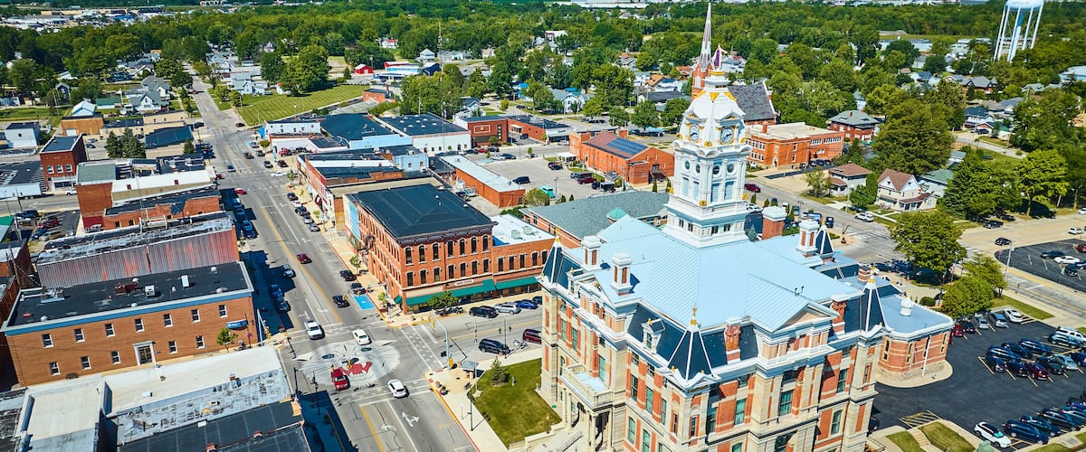 An aerial view of a town with a prominent clock tower, a large water tower, and a mix of historic and modern buildings.