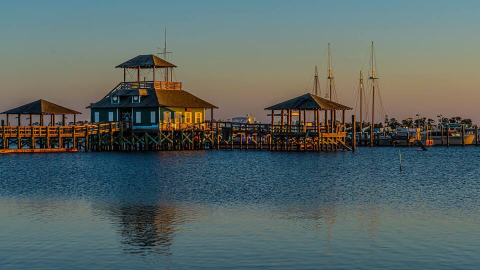 A pier with wooden structures and a lighthouse at sunset.