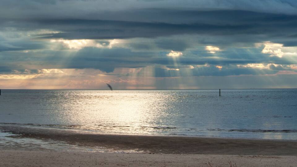 A beach with a cloudy sky and sunlight reflecting on the water.