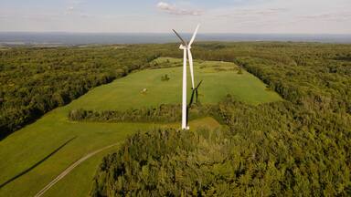 Aerial view of wind turbines in a scenic rural landscape with fields and forests under a cloudy sky, Lowville, United States of America.