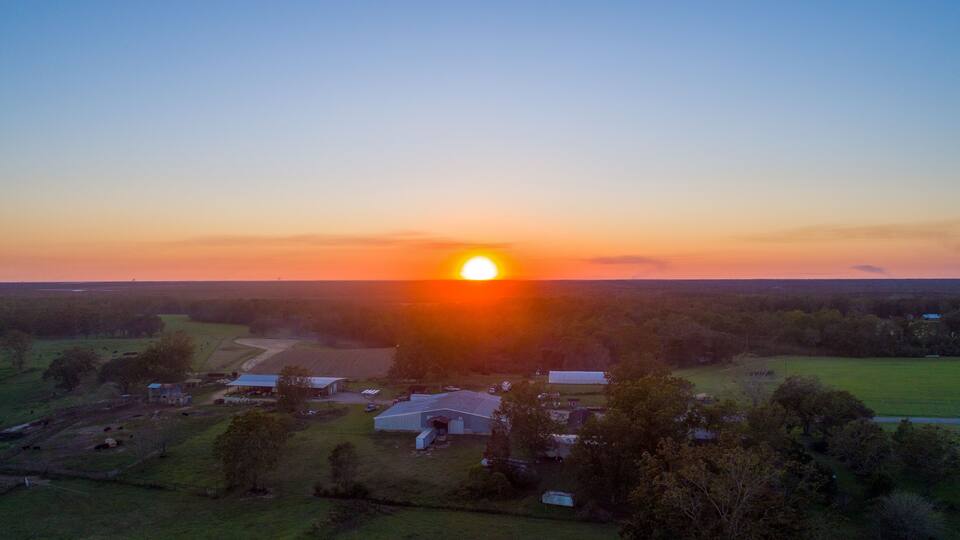 A sunset over a rural landscape with fields, a few buildings, and scattered trees.