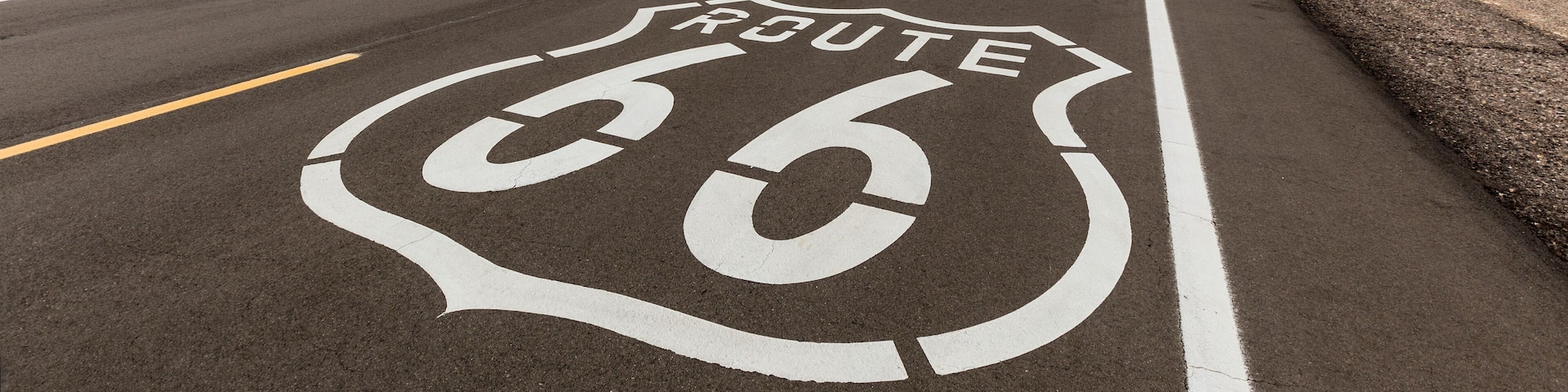 A road with Route 66 markings, surrounded by desert landscape and mountains.