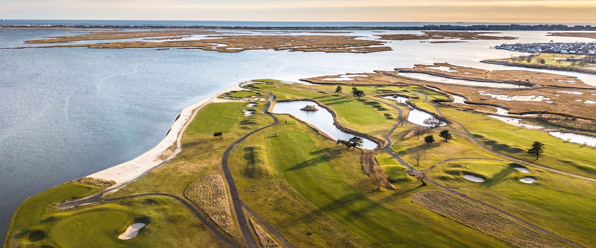 An aerial view of a coastal golf course with water bodies and a distant town.