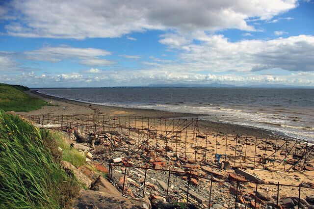 Una playa rocosa con una valla de metal y una zona cubierta de césped.