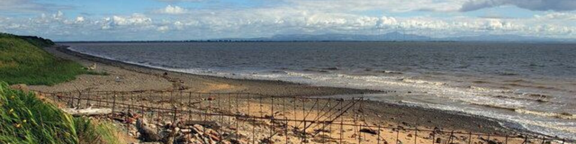 Una playa rocosa con una valla de metal y una zona cubierta de césped.