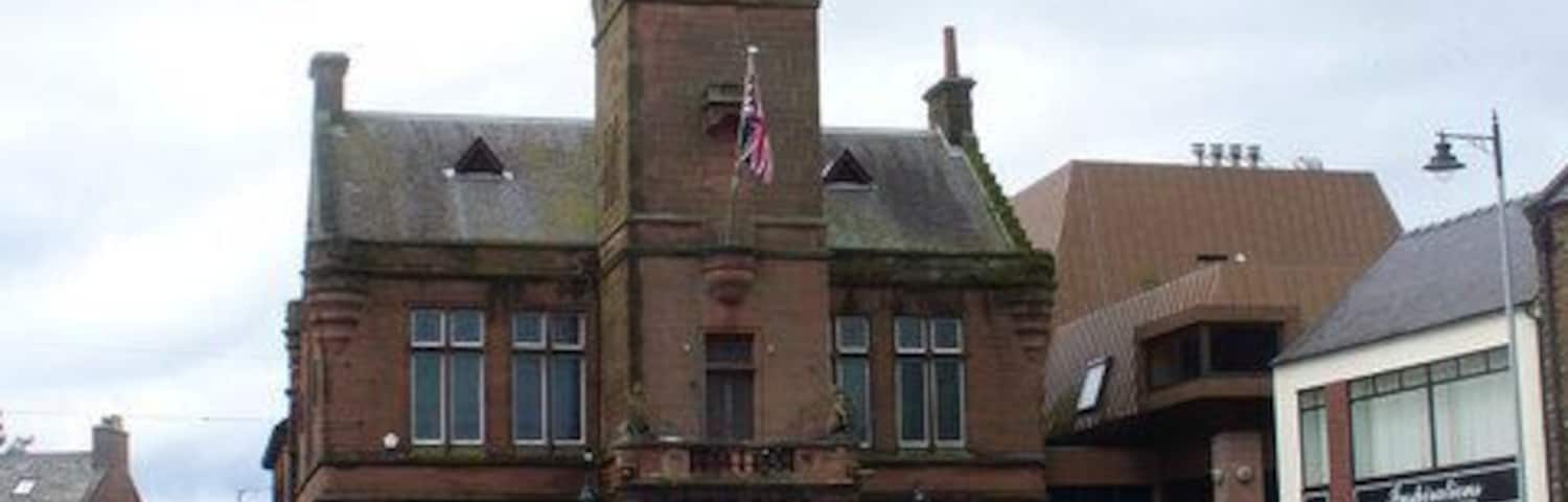 Un edificio histórico con una torre de reloj, rodeado de flores coloridas y automóviles estacionados.