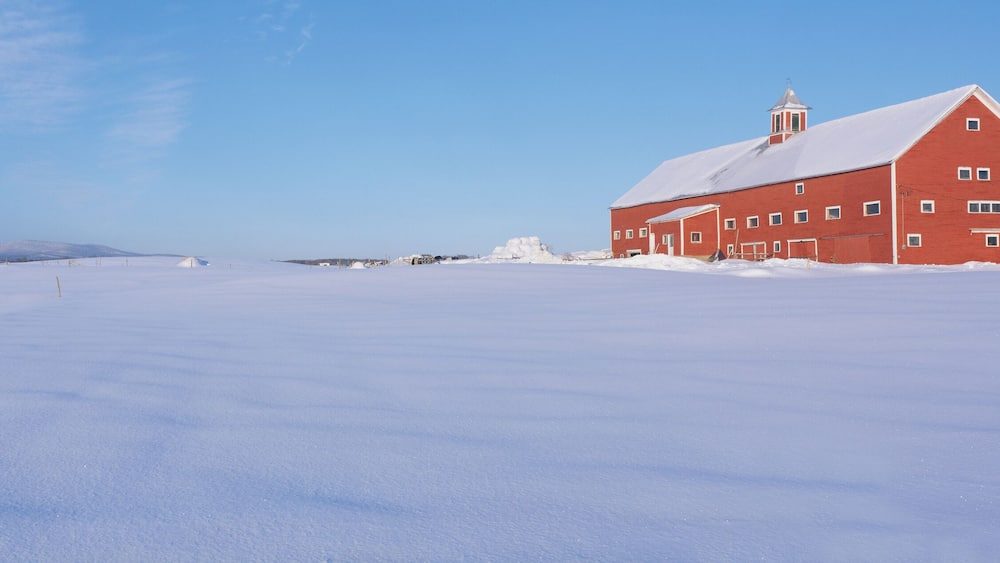 Ein rotes Bauernhaus auf einem verschneiten Feld, bewölkter, blauer Himmel.