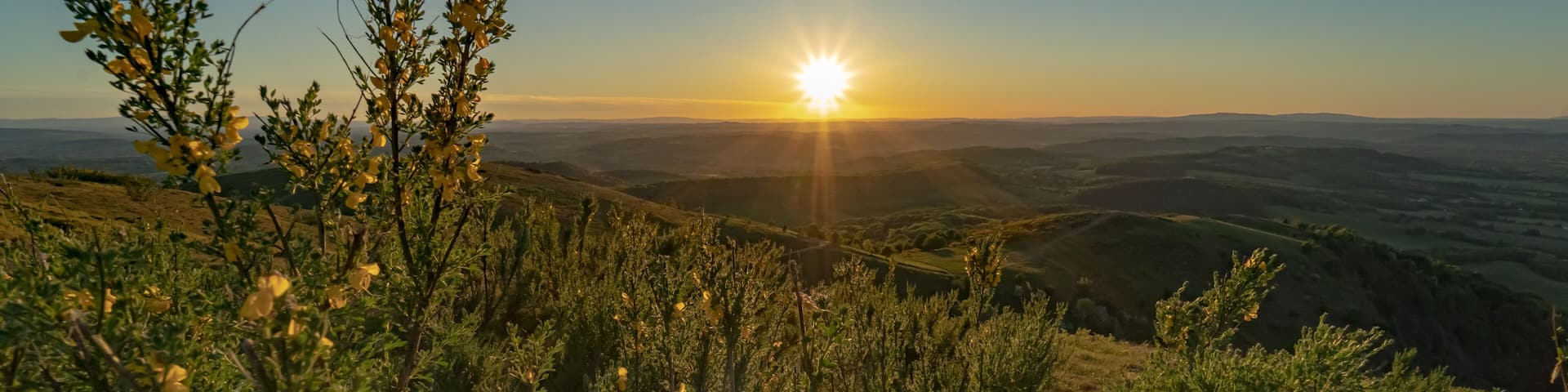 A sunset over rolling hills with sparse vegetation.