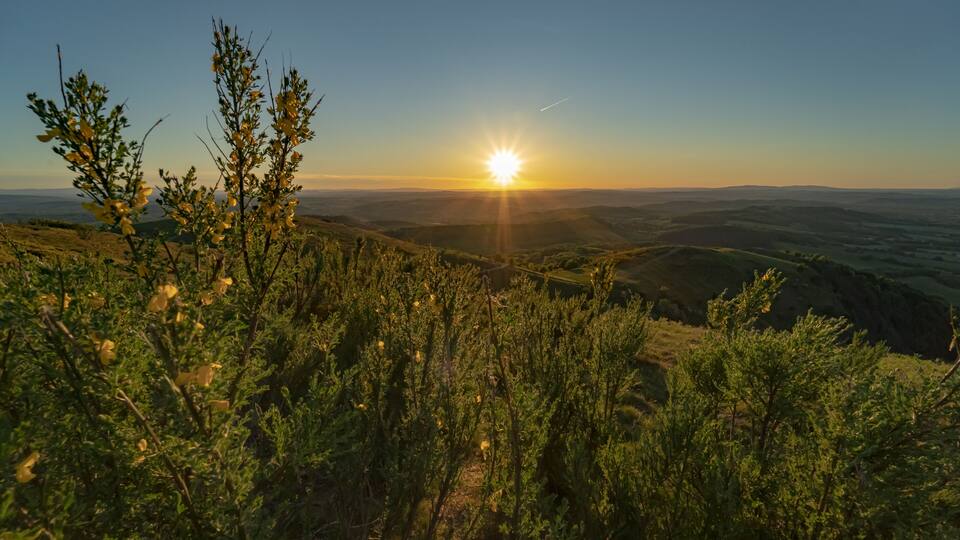 A sunset over rolling hills with sparse vegetation.