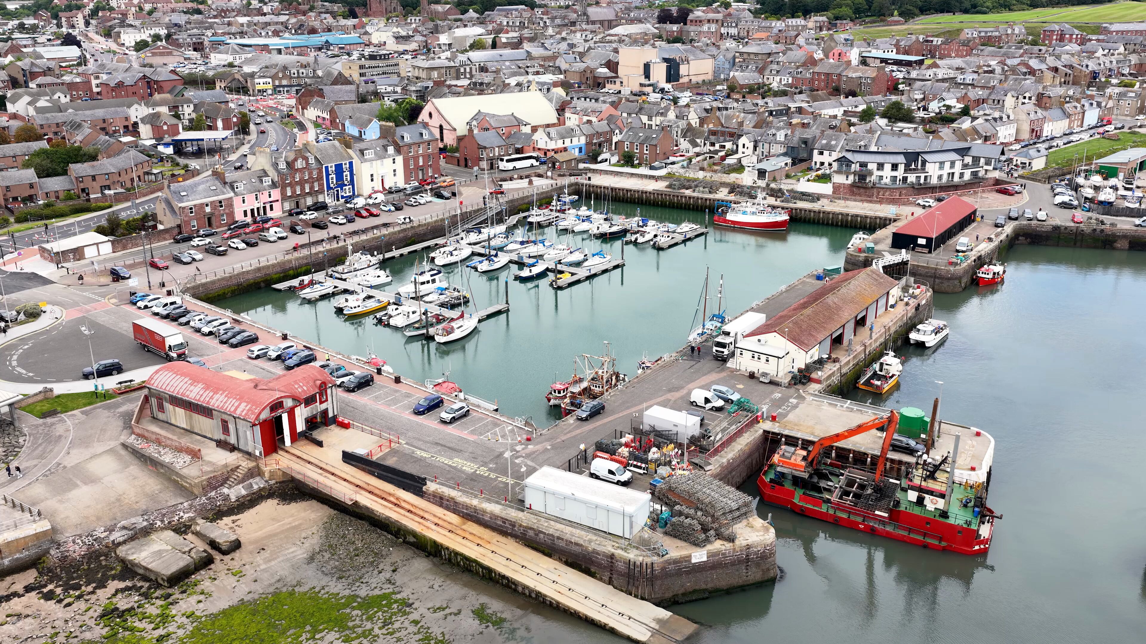A harbor with boats, a large red ship, and a town with buildings.