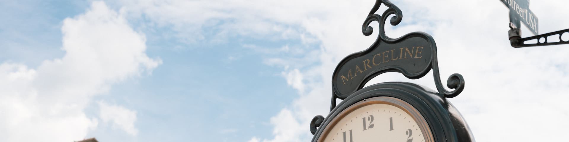 A clock with a sign reading 'Main Street USA' and a building with a brick facade in the background.