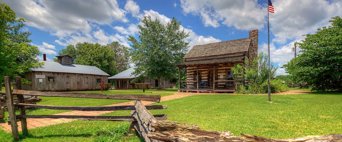 A rustic log cabin with a wooden fence and a flagpole with an American flag.