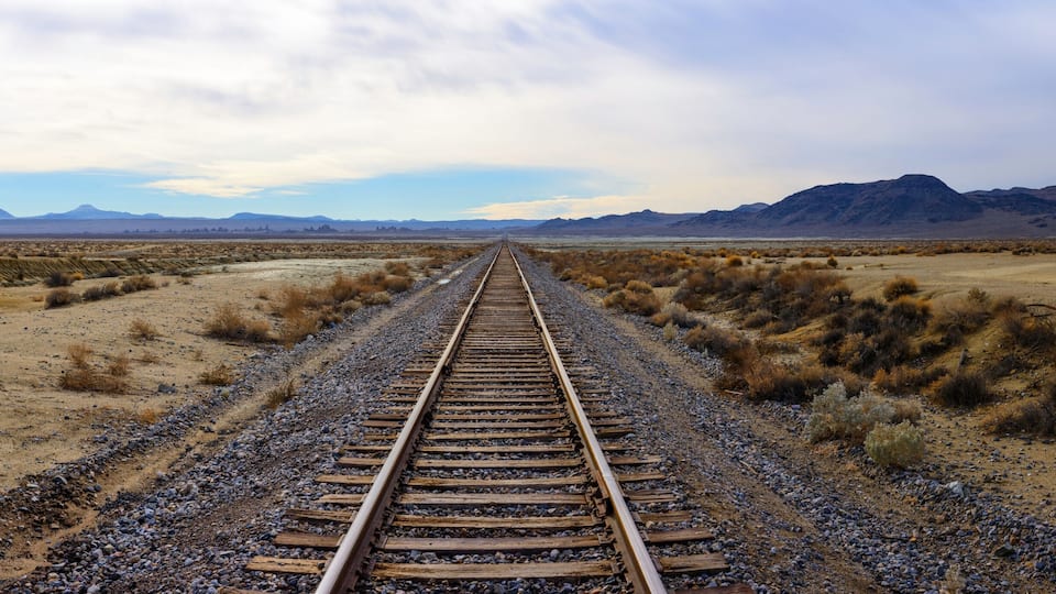 A railway track extending into a desert landscape with mountains in the distance.